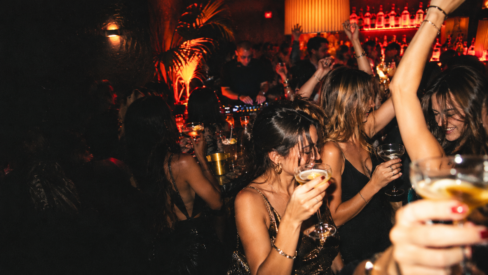 A packed cocktail bar at night with friends dancing and a DJ playing